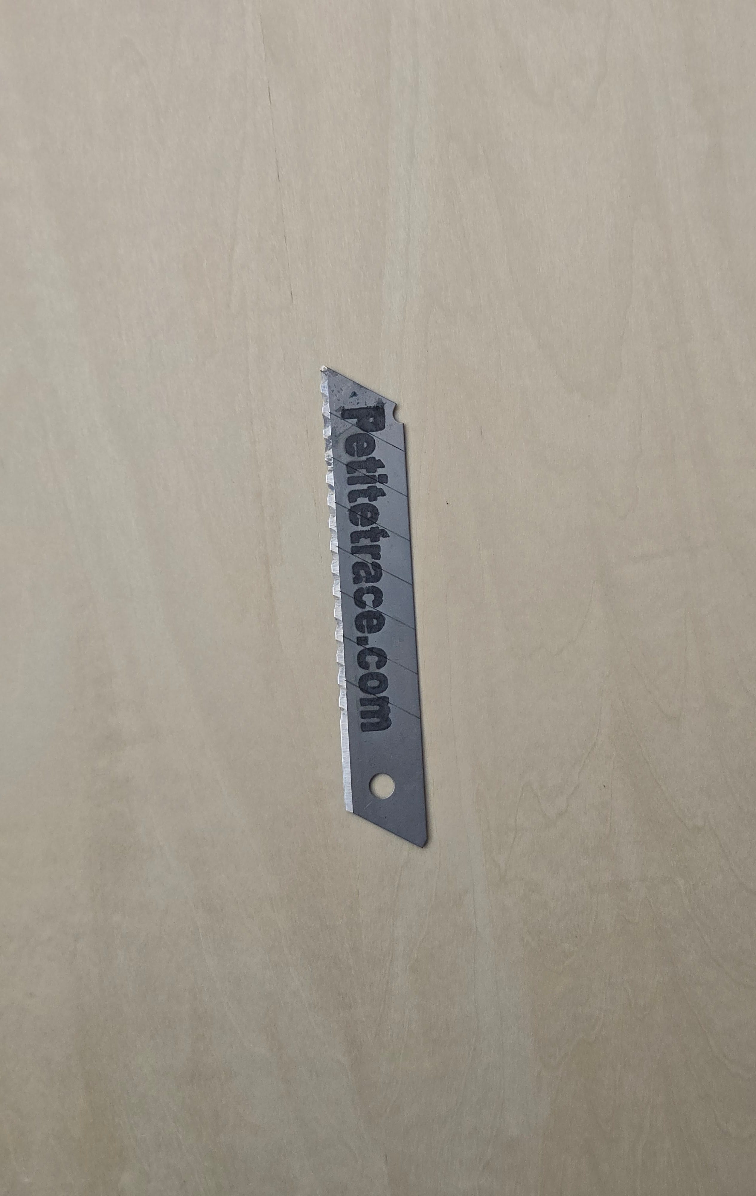 Petitetrace.com branded utility knife blade on a light wood background