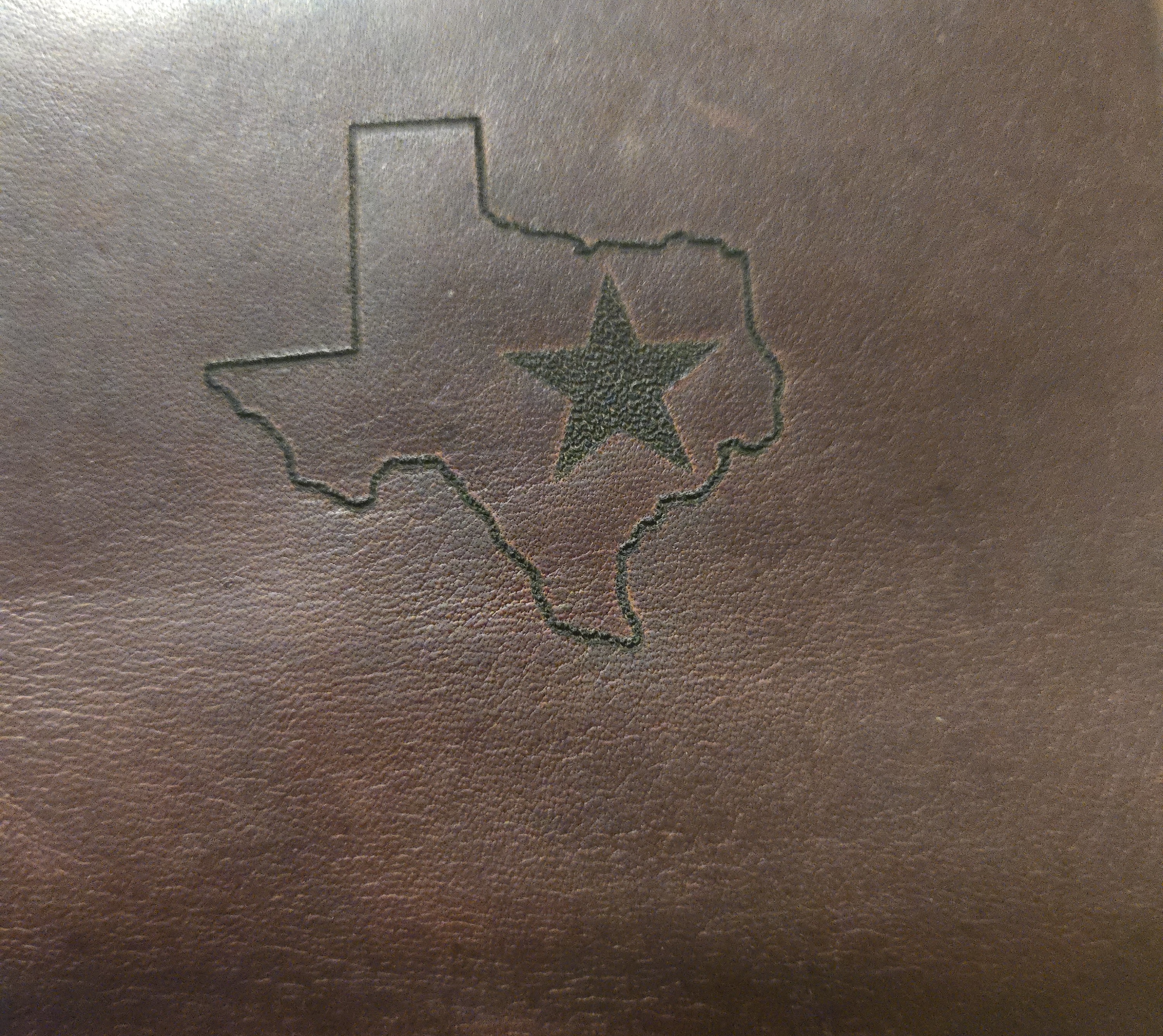 Laser-engraved Texas state outline with star on a brown leather surface by PetiteTrace