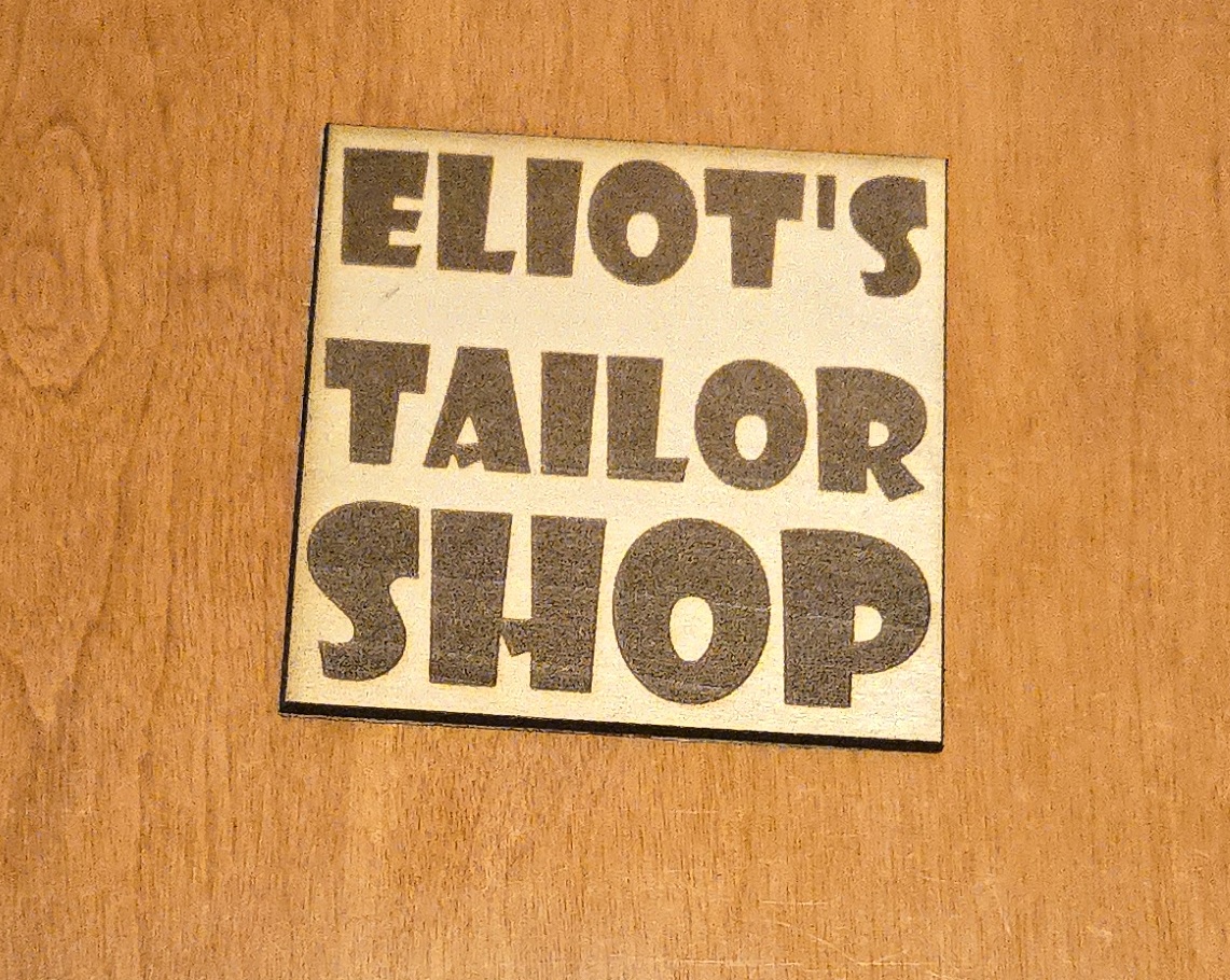 Custom laser-cut wooden sign for 'Eliot's Tailor Shop' by PetiteTrace