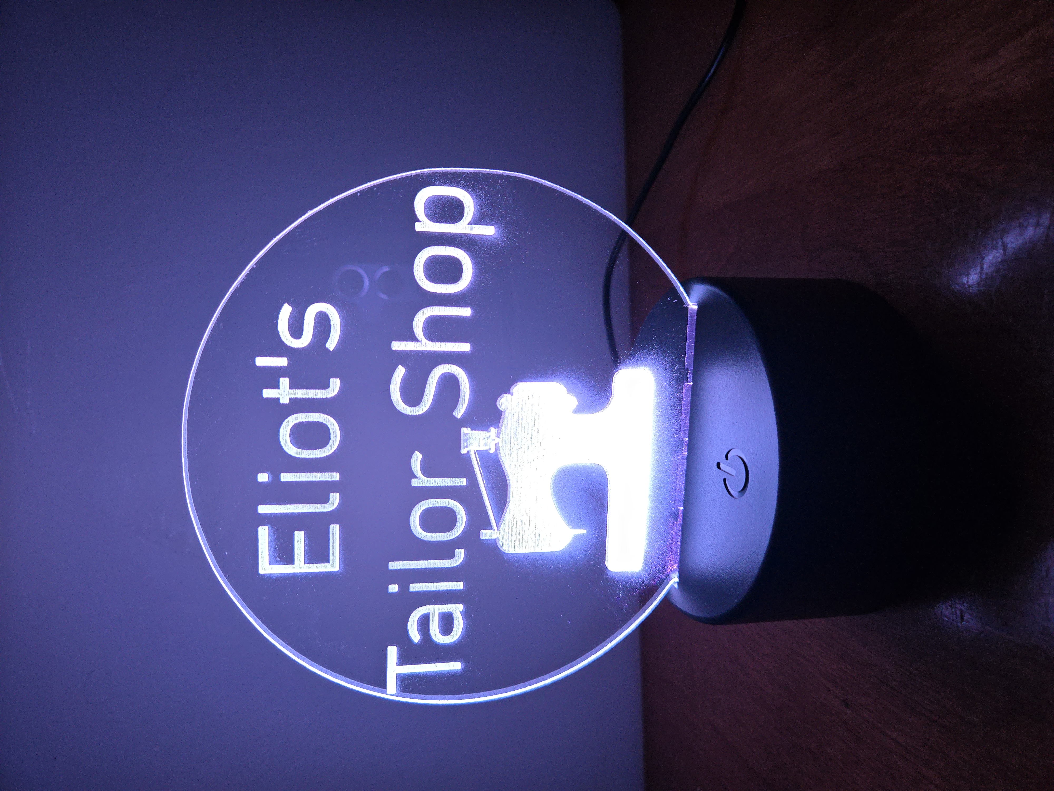 Custom LED acrylic night light sign for 'Eliot's Tailor Shop' with sewing machine icon, illuminated in blue by PetiteTrace