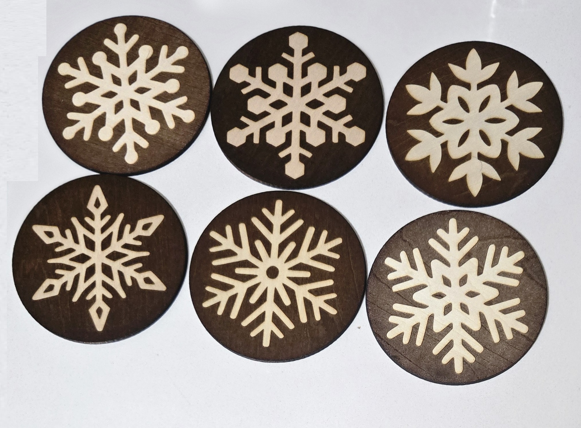 Set of six dark wooden coasters with various laser-engraved snowflake designs by PetiteTrace